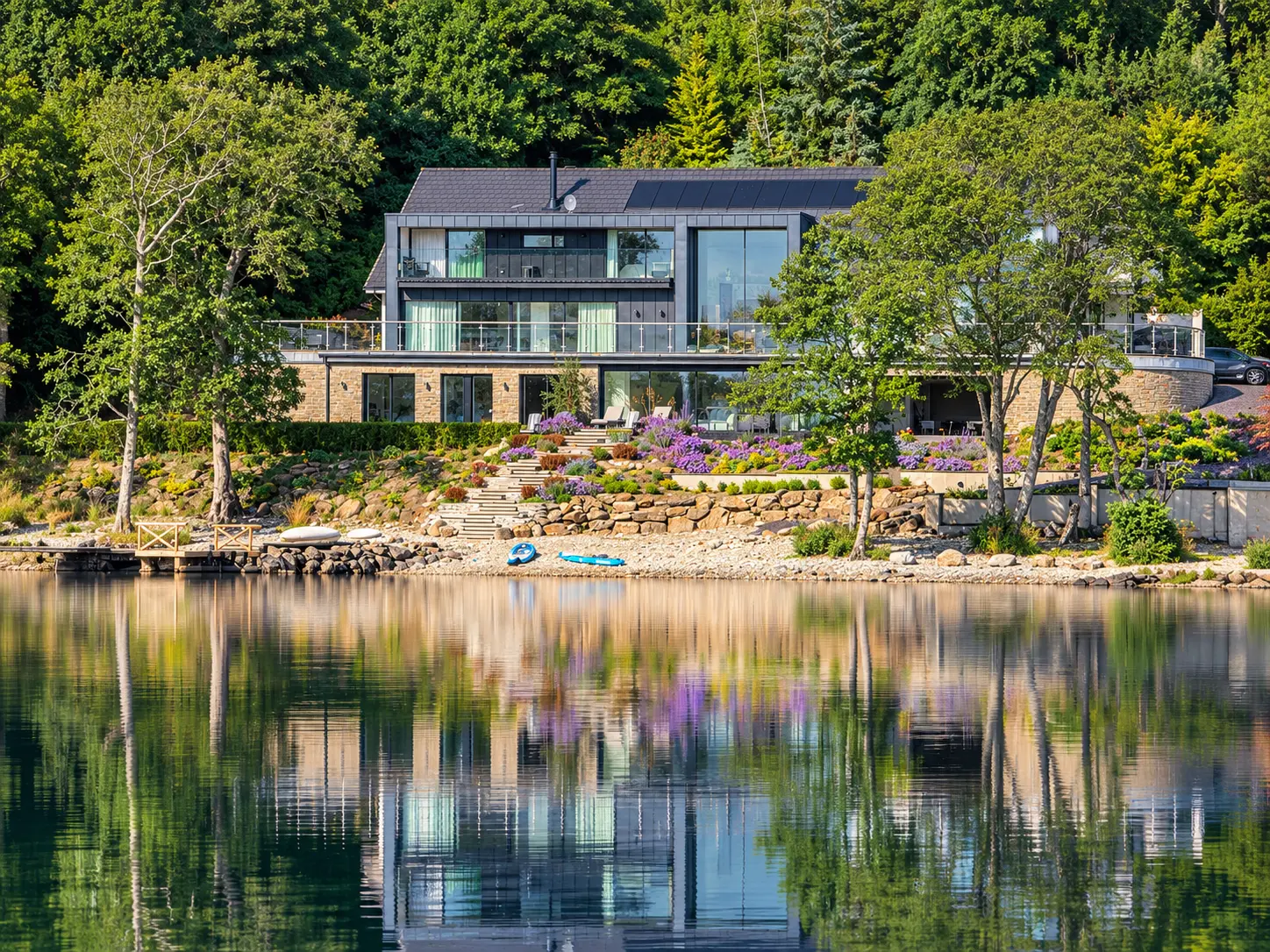 The Moorings in summer with flowering terraced gardens, private jetty and paddleboards on the shore of Loch Tay