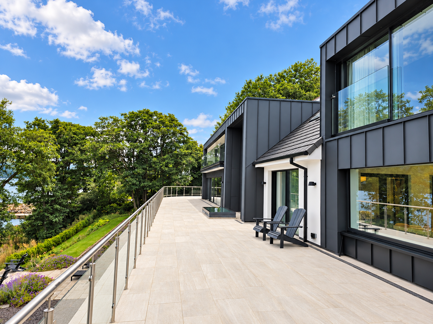 Wide upper terrace with glass balustrade and Adirondack chairs beside the zinc-clad house