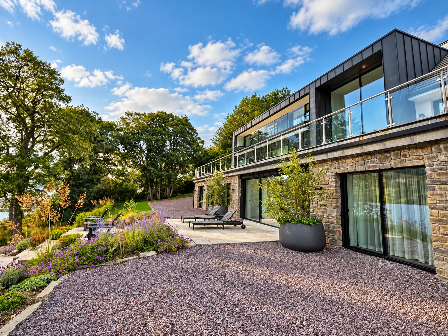 Stone and zinc-clad house with sun loungers, planted borders and slate garden