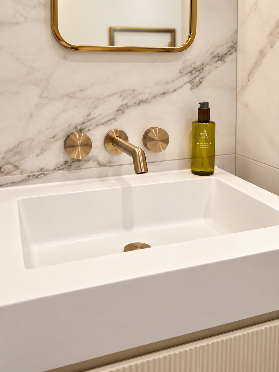 Brushed brass wall tap above a white basin against marble