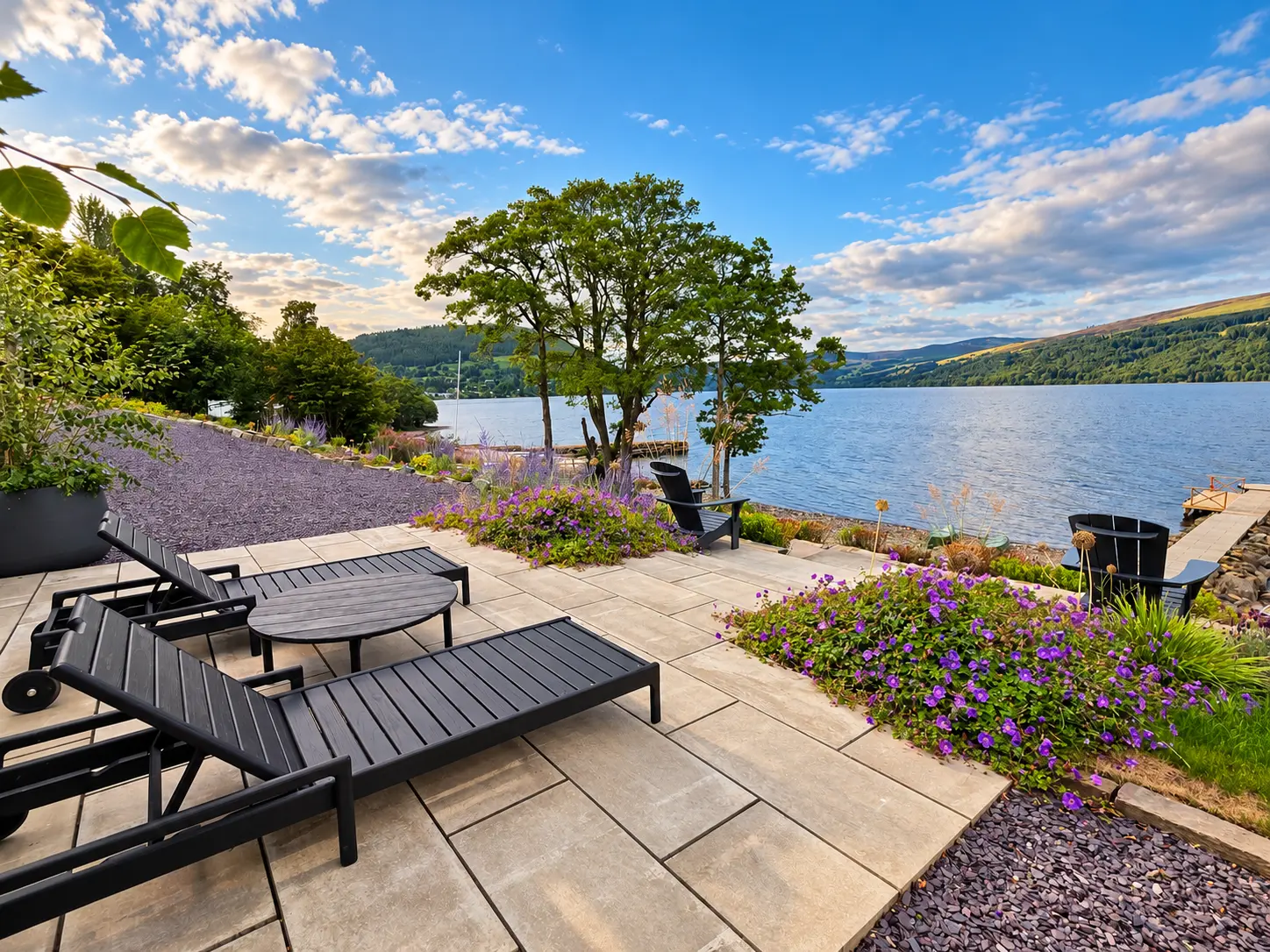 Stone terrace with sun loungers and flowering borders overlooking Loch Tay