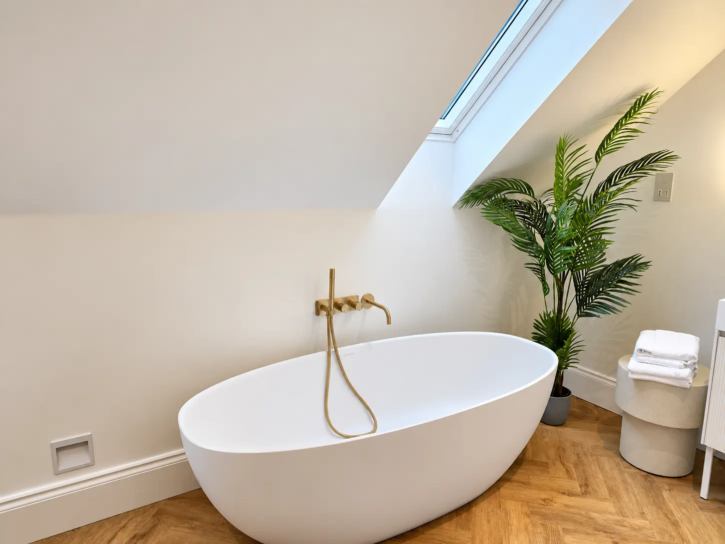 Freestanding bath with brass taps beneath a skylight