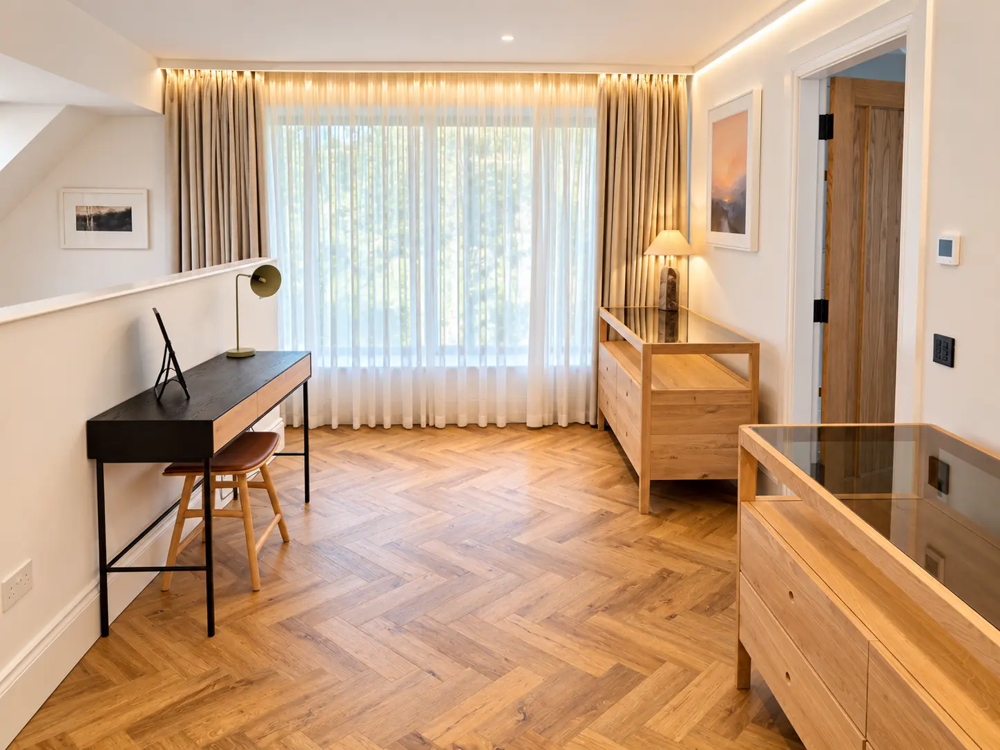 Bright upstairs bedroom with herringbone oak floor, oak chests and a writing desk beside a window looking over the garden