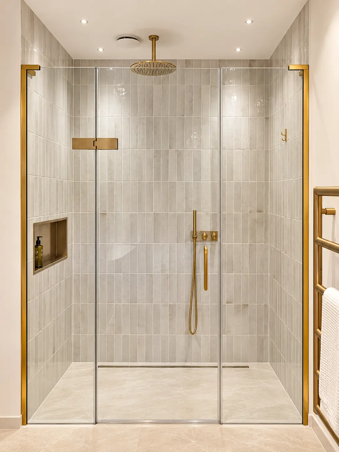 Walk-in shower with brushed brass rainfall head, glazed screen and heated towel rail
