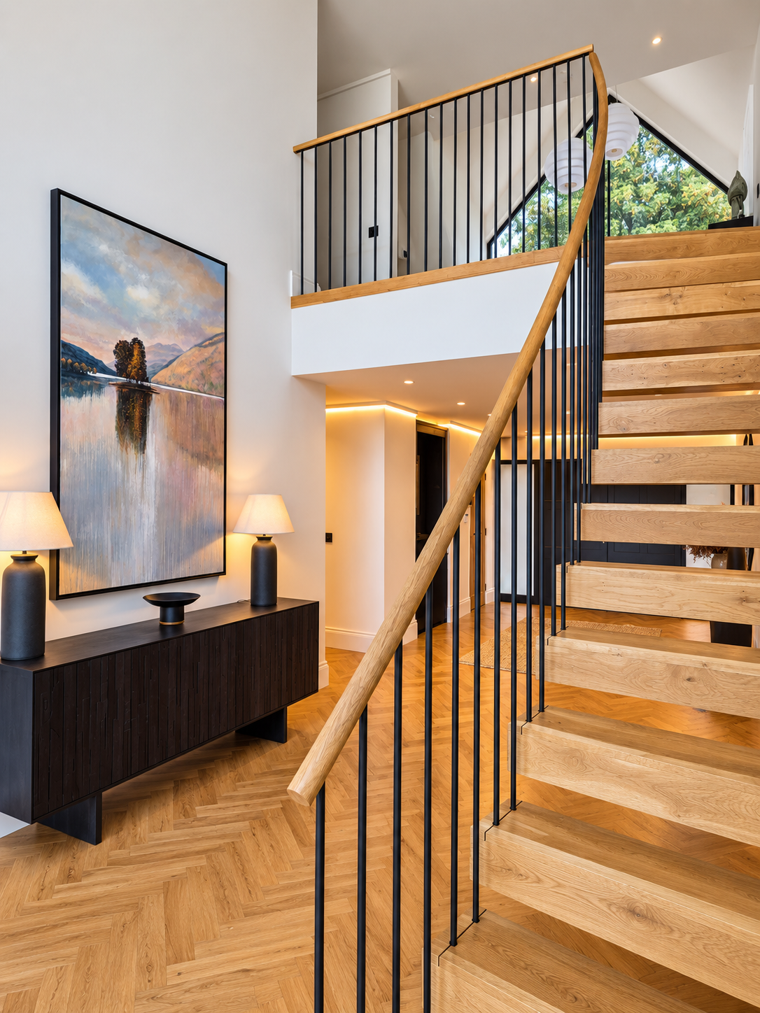 Curving oak staircase with black balusters in a double-height hall