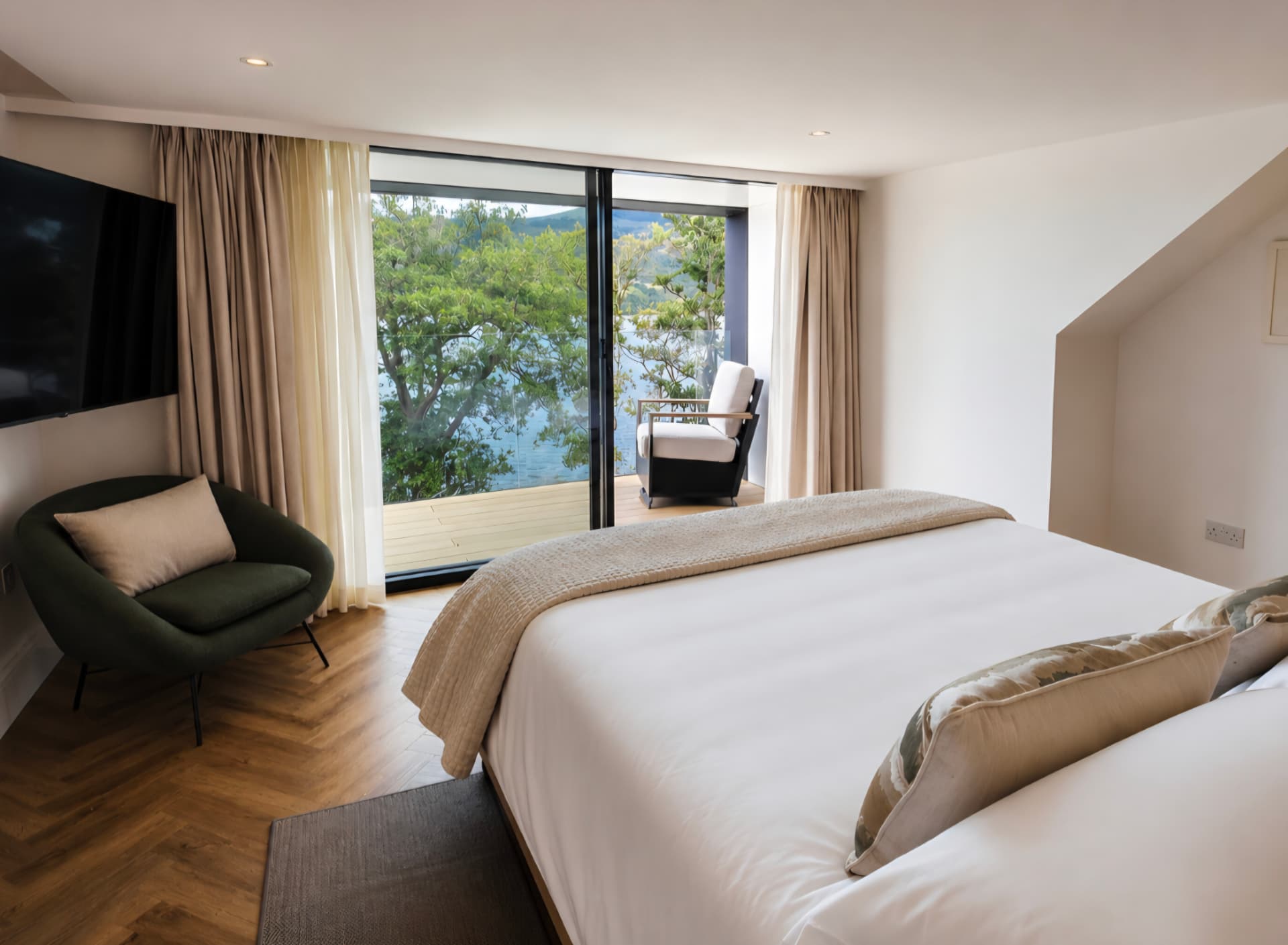 Bedroom with green armchair, wall-mounted TV and sliding doors onto a balcony over the loch